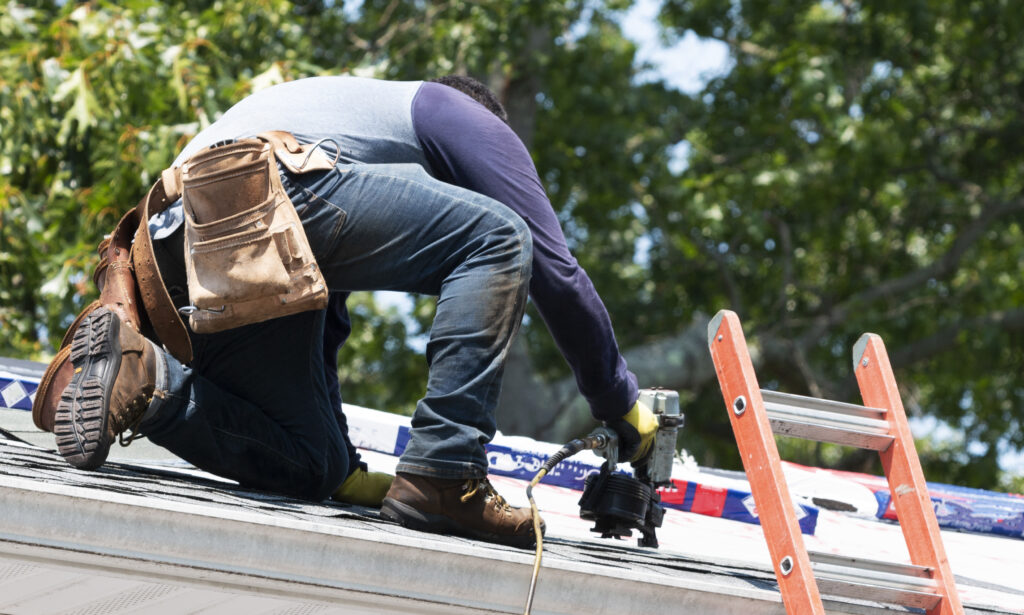 A roofer in Chesterfield, MO, is kneeling on a residential roof. 